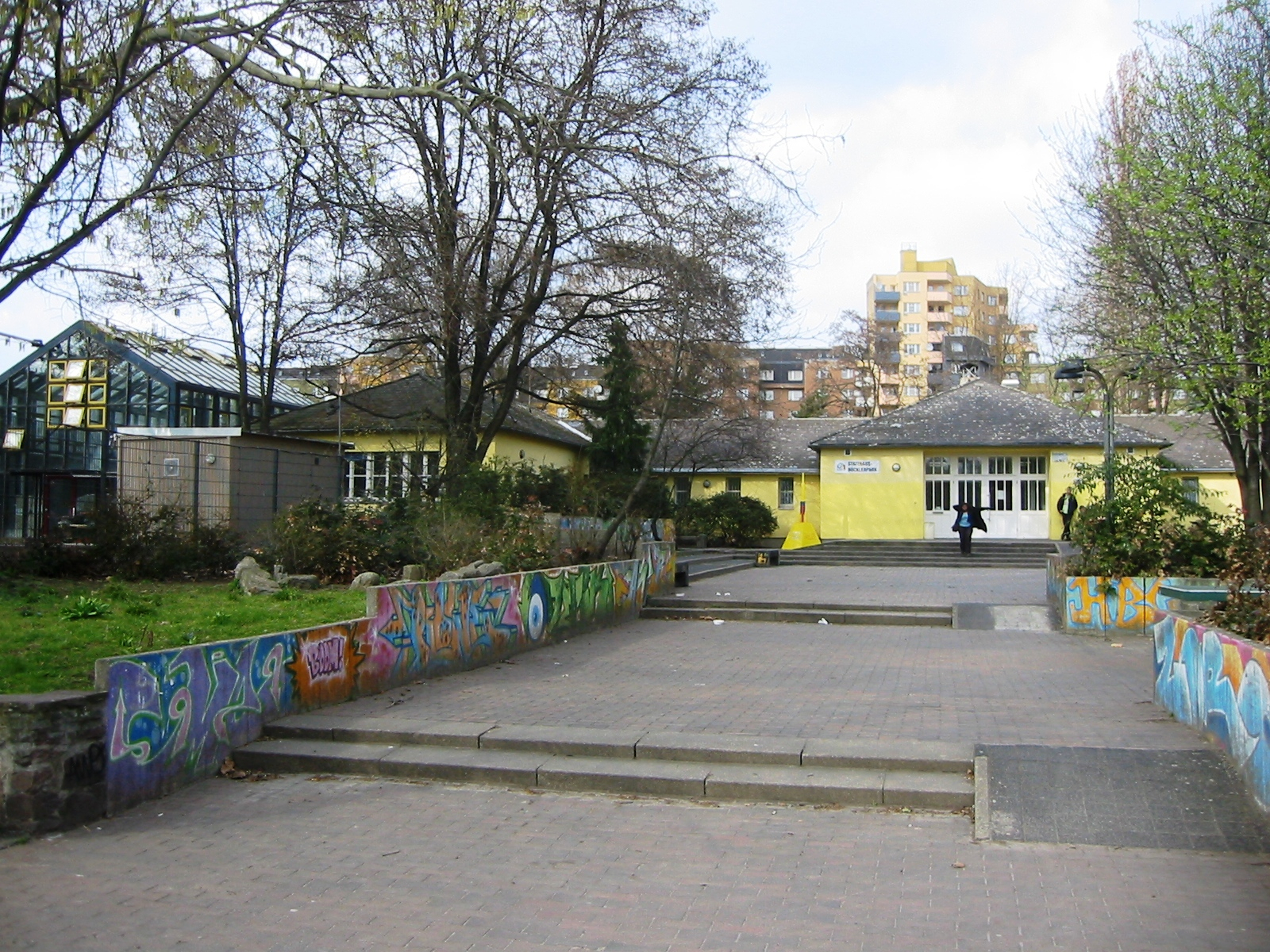 © Assenmacher, CC BY-SA 3.0 <https://creativecommons.org/licenses/by-sa/3.0>, via Wikimedia Commons A paved, wide path leads to the entrance of the Statthaus Böcklerpark.
