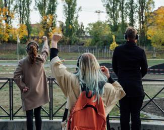 © Lukas Probst Menschen mit Kopfhörern stehen vor einem Geländer im Park und recken die Faust.