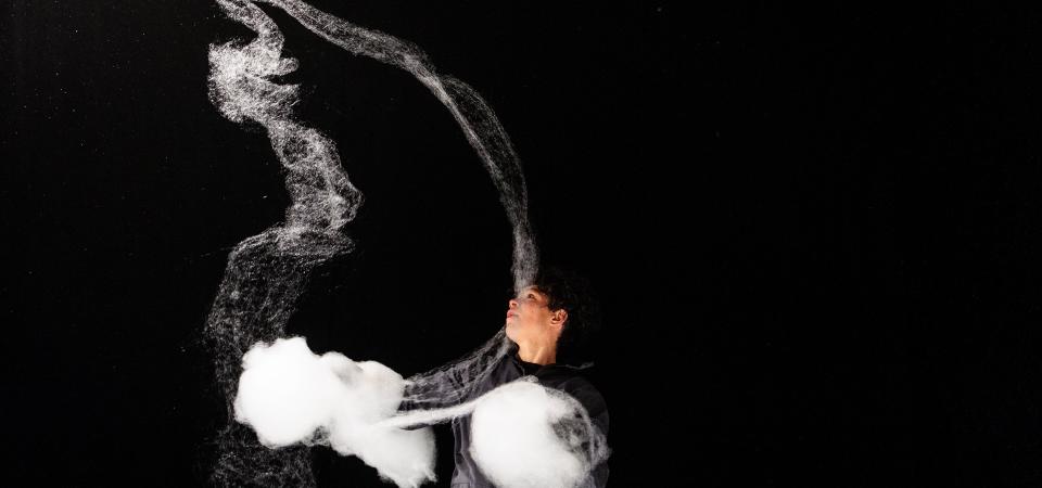 © Peter van Heesen - Schloss Bröllin Eine Frau, schwarz gekleidet vor einem schwarzen Hintergrund, spielt mit Zuckerwatte